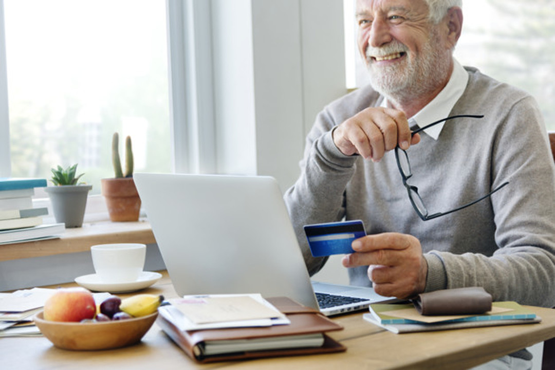 Homem sentado em frente a um notebook com livros e cadernos à sua frente segurando o cartão Santander Unlimited