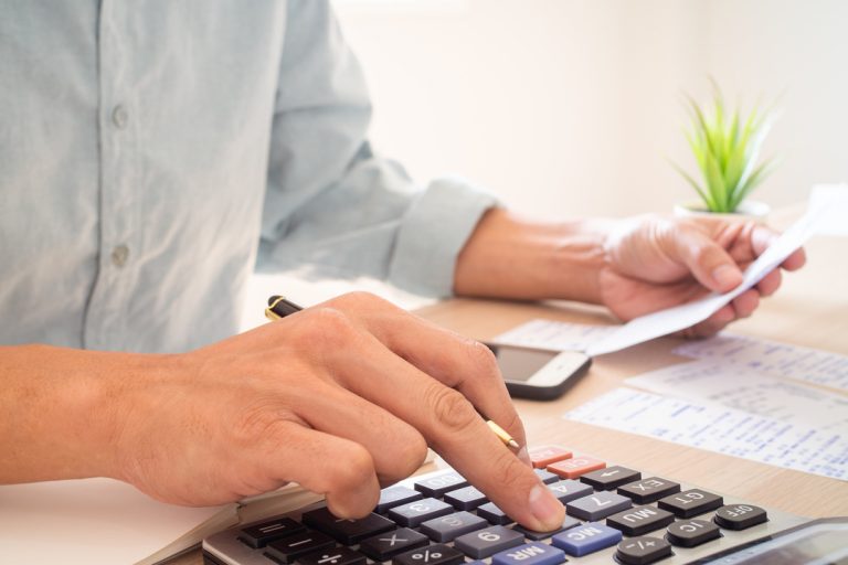 Home segurando em uma mão um cheque internacional e com a outra mão usando a calculadora