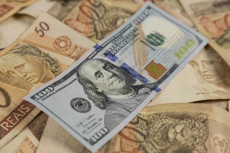 converter dólar em real: Nota de 100 dólares em cima de notas de 50 reais