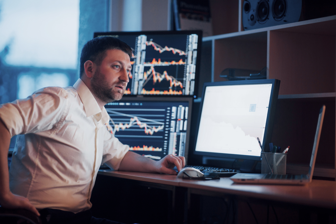 O que é day trade: homem sentado em frente a uma mesa com computadores.