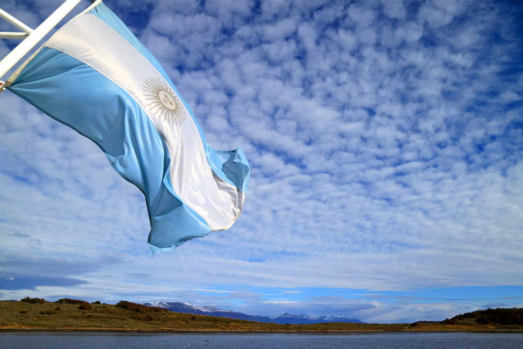 Bandeira no topo de um mastro balançando com o céu ao fundo.