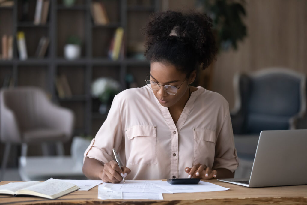 Mulher em um escritório com notebook, calculadora e documentos na mesa, declarando IR 2022