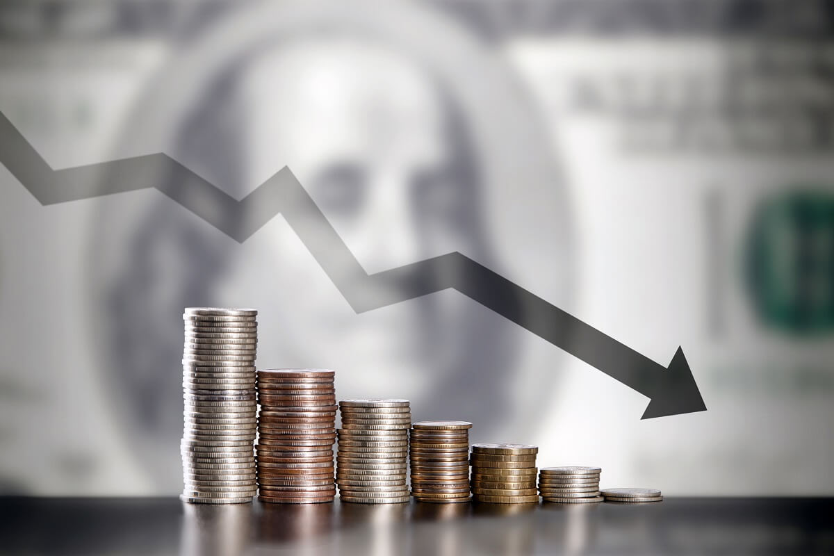 Nota de dólar ao fundo e um gráfico em queda na frente em cima de fileiras de moeda