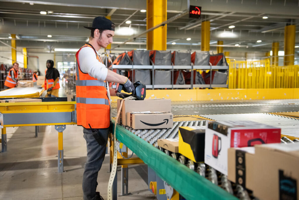 Rapaz na esteira do Centro de Distribuição da Amazon etiquetando caixas.