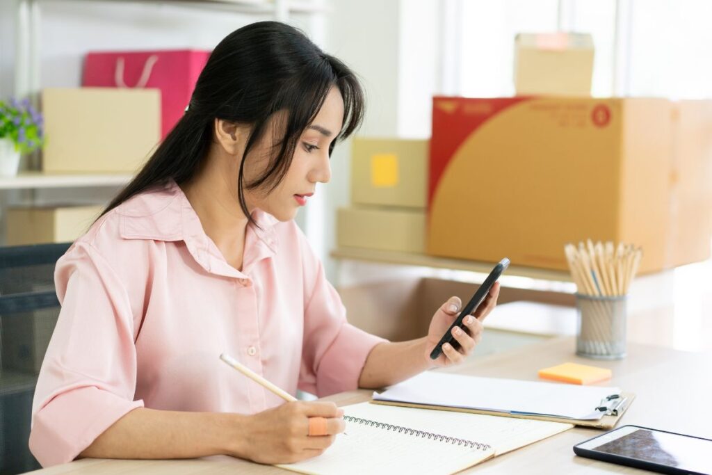 Mulher conferindo os pedidos online e anotando no papel.