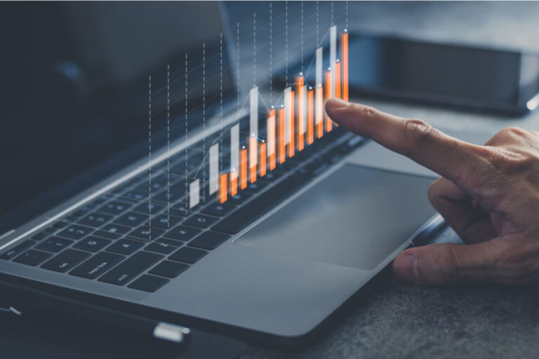 Imagem de um notebook e um gráfico de crescimento sendo projetado, com uma mão humana apontando para ele