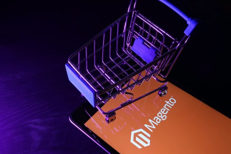 Celular com o logo do Magento na tela e um carrinho de compras em cima.