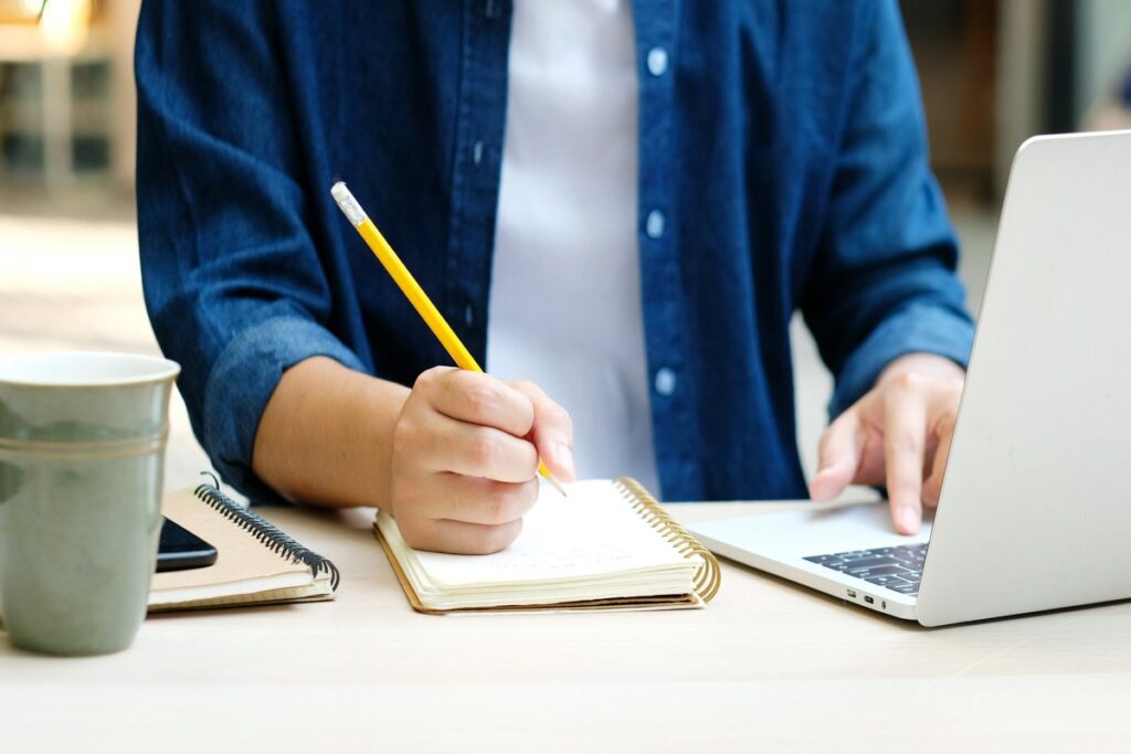 Mãos de homem escrevendo no papel e usando o notebook