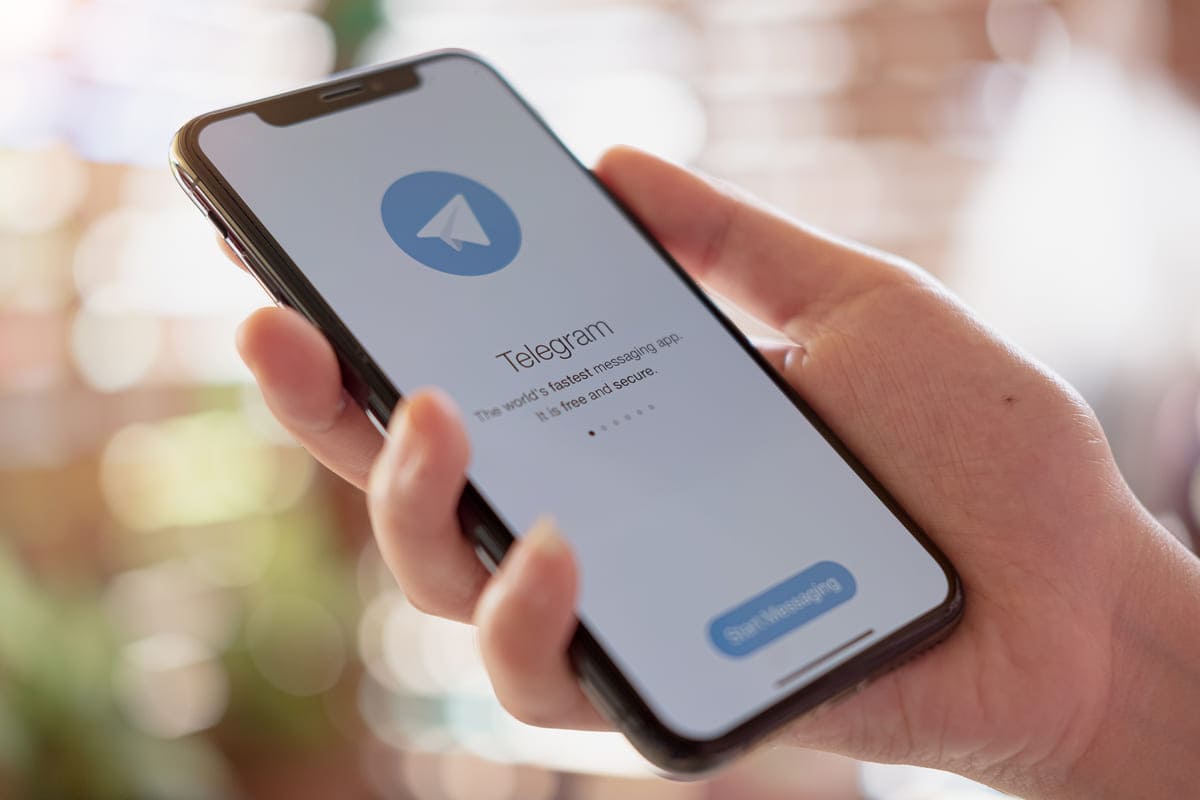 Uma mão de uma pessoa branca segurando um celular enquanto acessa o Telegram.