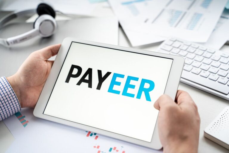 Homem no escritório olhando para o tablet com logo do Payeer.