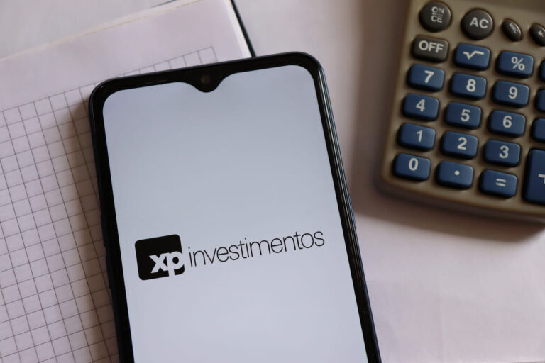 Telefone em cima de uma mesa exibindo em sua tela o app XP Investimentos, onde será possível solicitar a conta global XP